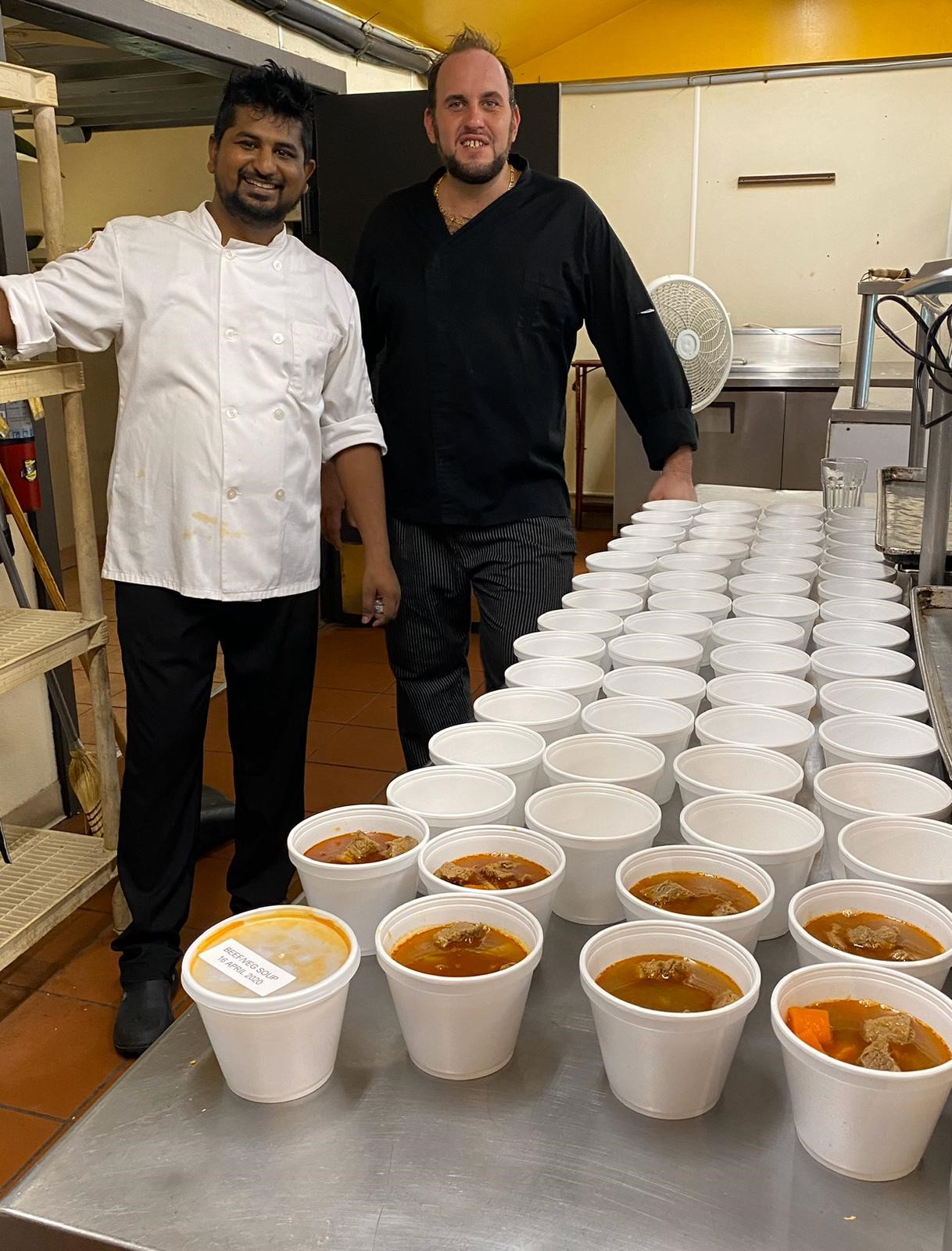 two-chefs-standing-behind-a-row-of-beef-soup-in-a-kitchen